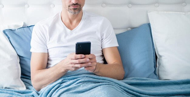 Volwassen man in bed aan het chatten op de telefoon