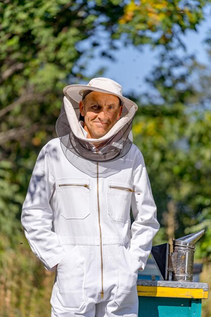 Volwassen man in beschermend uniform staat in de buurt van bijenkorven. Imker doet zijn werk met honingoogst.