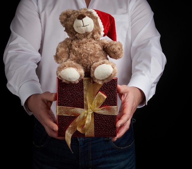 Volwassen man in een wit shirt heeft een rode vierkante doos vastgebonden met een gouden lint en een bruine teddybeer