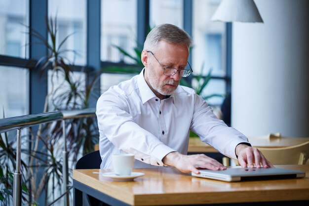 Volwassen man in glazen manager zakenman werkte met succes en drinkt aan het eind van de dag koffie zonder jas