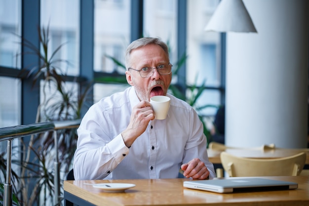 Volwassen man in glazen manager zakenman werkte met succes en drinkt aan het eind van de dag koffie zonder jas