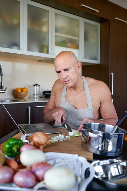 Volwassen man in keuken bereiden van voedsel en onderzoekt laptop