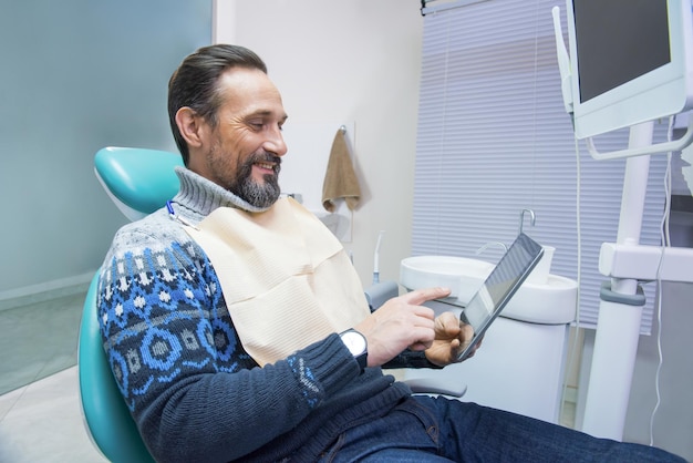 Volwassen man in tandartspraktijk volwassen man met tablet glimlachen