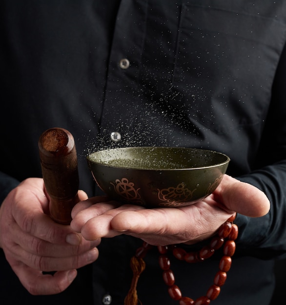 Volwassen man in zwart overhemd draait een houten stok om een koperen Tibetaanse kom met water. ritueel van meditatie