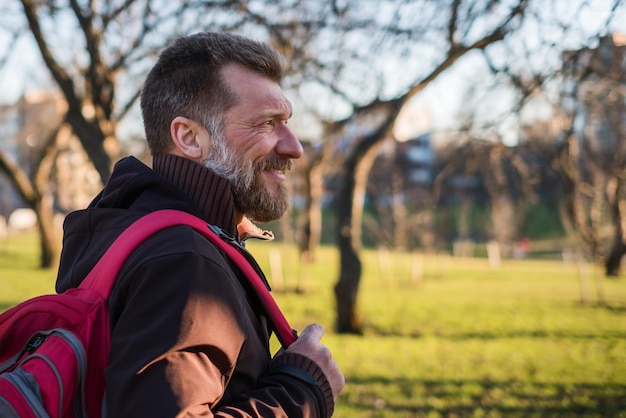 Volwassen man loopt op een zonnige dag in een park met een rugzak en lacht