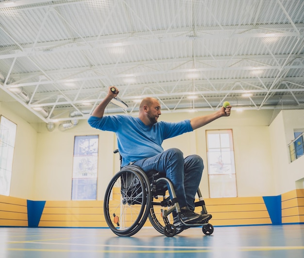 Volwassen man met een lichamelijke handicap die rolstoeltennis gebruikt op een indoortennisbaan
