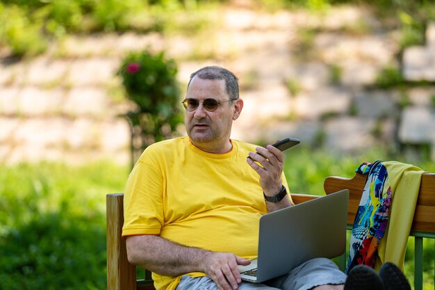 Volwassen man met laptop en smartphone aan het werk buiten in een tuin groen kantoor aan huis concept