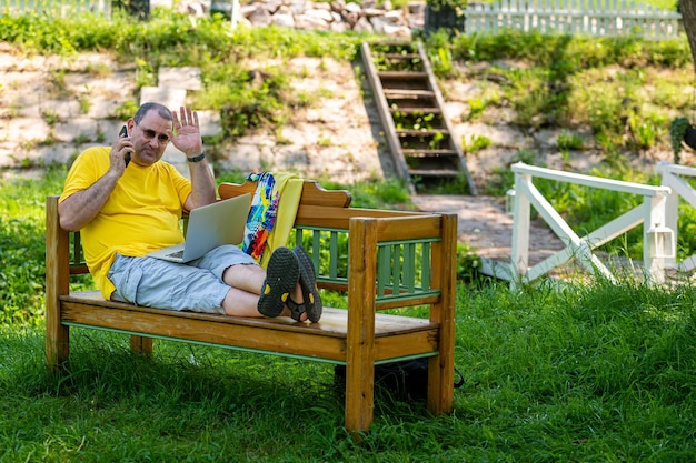 Volwassen man met laptop en smartphone aan het werk buiten in een tuin groen kantoor aan huis concept