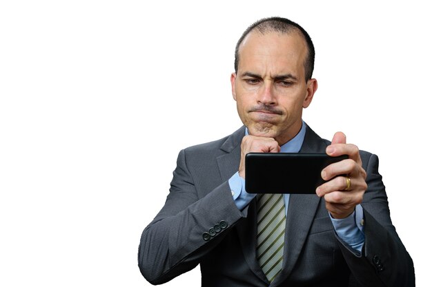 Volwassen man met pak en stropdas, kijkend naar zijn smartphone, teleurgesteld en met zijn vuist onder de kin.