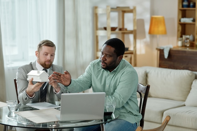 Volwassen man mockup huis te houden en zwarte man op woningkrediet zittend aan tafel te adviseren