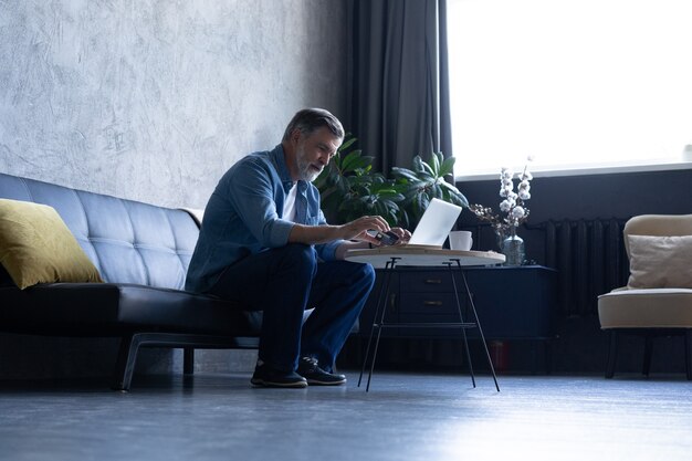 Volwassen man online winkelen op laptop, met behulp van creditcard thuis.