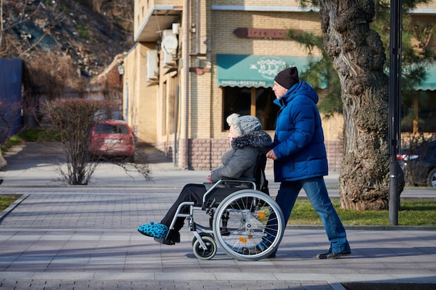 Volwassen man rolt zijn gehandicapte moeder op rolstoel zorgvuldige relatie met gehandicapte