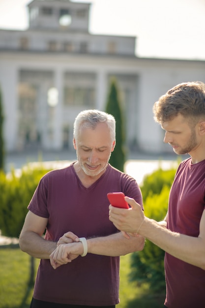 Volwassen man smartwatch met jonge mannelijke bedrijfsmartphone controleren