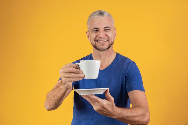 Volwassen man van middelbare leeftijd met een kopje koffie of thee op gele achtergrond met vrije ruimte voor tekst