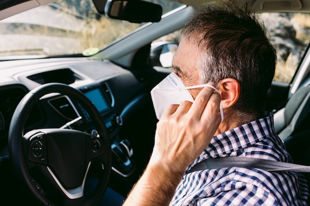 Volwassen man zet masker op in auto om zichzelf tegen covid-19 te beschermen