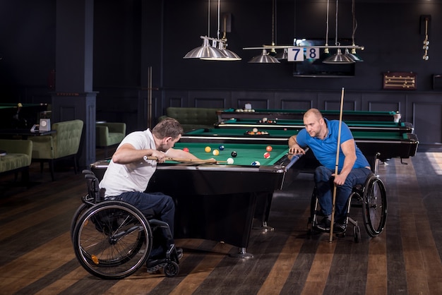 Volwassen mannen met een handicap in een rolstoel spelen biljart in de club
