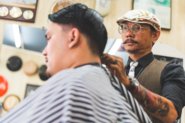 Volwassen mannen stijlvolle haarstylist met tatoeages en snor knippen haar van klant in kapperszaak