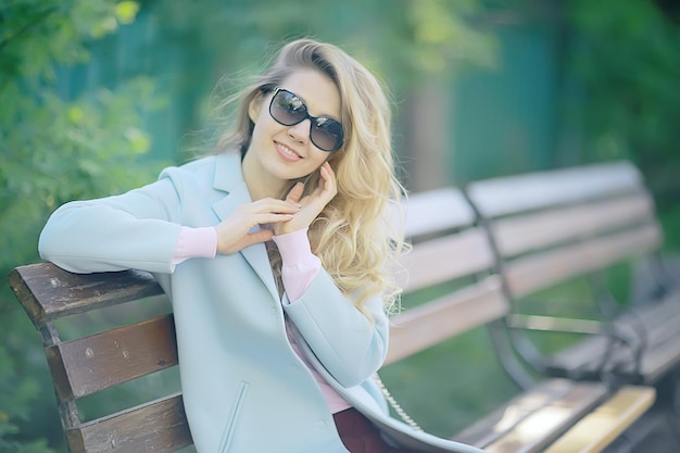 volwassen meisje zittend op een bankje in het park / mooie modelvrouw rustend op een bankje, vrolijk gelukkig meisje