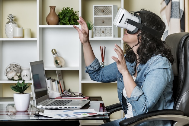 Volwassen ondergedompelde vrouw die virtuele werkelijkheidsglazen gebruiken terwijl thuis het zitten bij lijst met netbook
