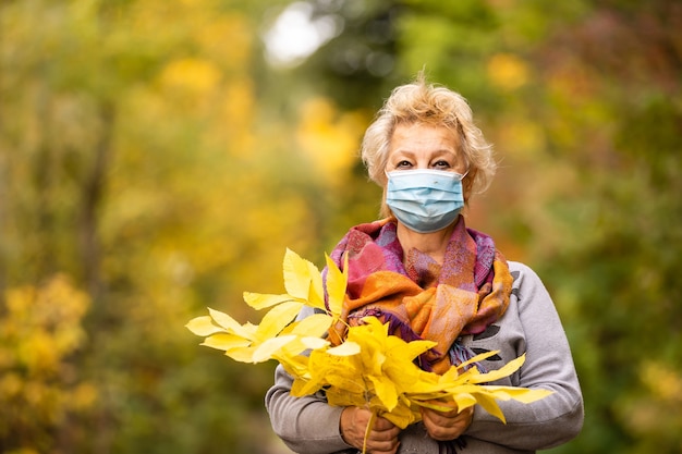 Volwassen oudere senior vrouw medisch beschermend masker in de herfst op straat. Zon en schaduw. Tegen houten achtergrond