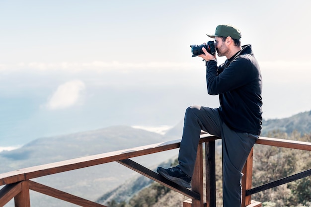 Volwassen persoon met een camera die op het uitkijkpunt zit en foto's maakt naar het landschap