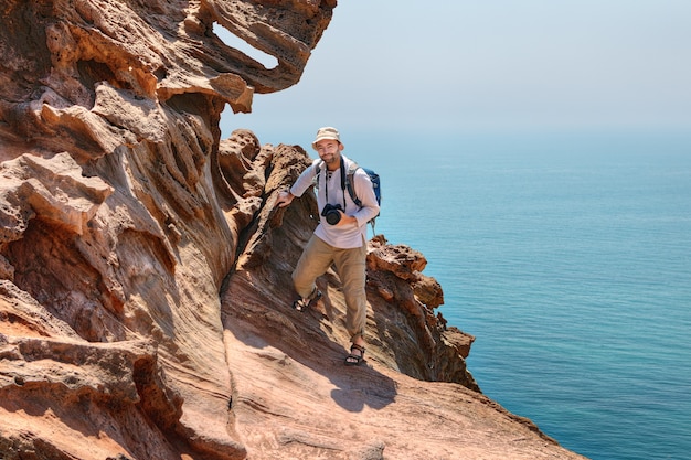 Volwassen reiziger fotograaf klimt op rotsen boven zee, Hormuz Island, Hormozgan, Iran.