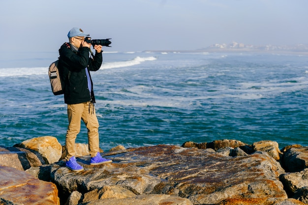 Volwassen reizigersmens die een foto van mooi landschap van oceaankaap in portugal met professionele camera in zonnige ochtend nemen.