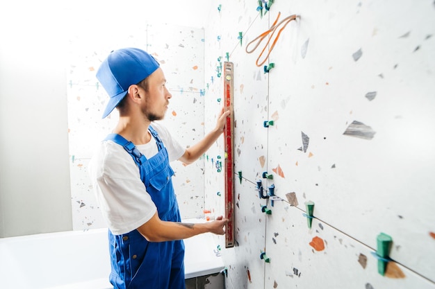 Volwassen reparateur in een speciaal uniform die tegels op de muur legt in de badkamer in een nieuw huis