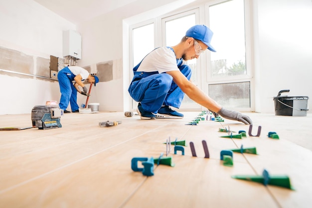 Volwassen reparateur in een speciaal uniform die tegels op de vloer legt in een nieuw huis