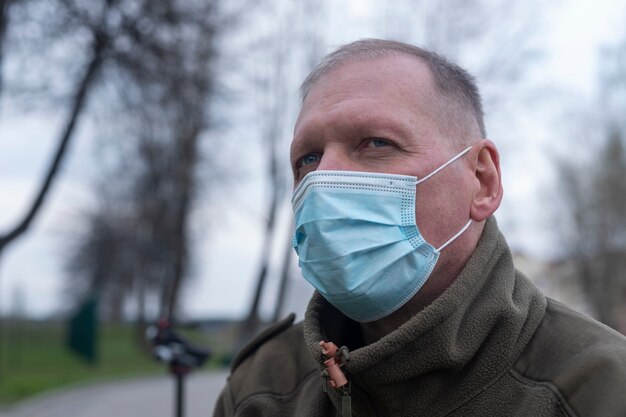 Volwassen senior man alleen in park in blauw gezichtsmasker.