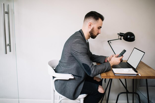 Volwassen stijlvolle man met smartphone aan balie in kantoor