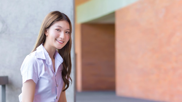 Volwassen thaise student in universiteitsuniform aziatische mooi meisje zittend op baksteen achtergrond