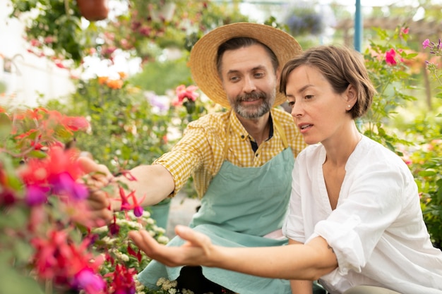 Volwassen tuinman die jonge vrouw nieuwe soorten bloemen in de serre toont en het aan haar beschrijft