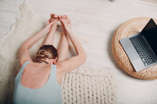 Volwassen volwassen vrouw die yoga doet in de woonkamer thuis met online tutorials op laptop