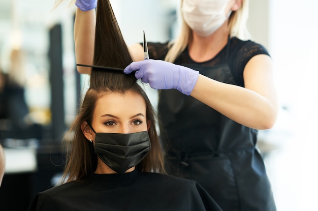 volwassen vrouw bij kapper die een beschermend masker draagt als gevolg van een pandemie van het coronavirus