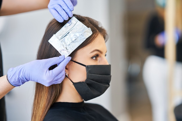 volwassen vrouw bij kapper die een beschermend masker draagt als gevolg van een pandemie van het coronavirus