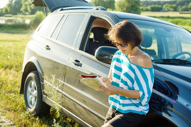 Volwassen vrouw die de toeristenkaart onderzoekt dichtbij auto