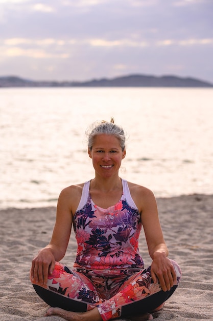 Foto volwassen vrouw die in lotushouding zit en yoga doet voor een gezonde levensstijl op het strand