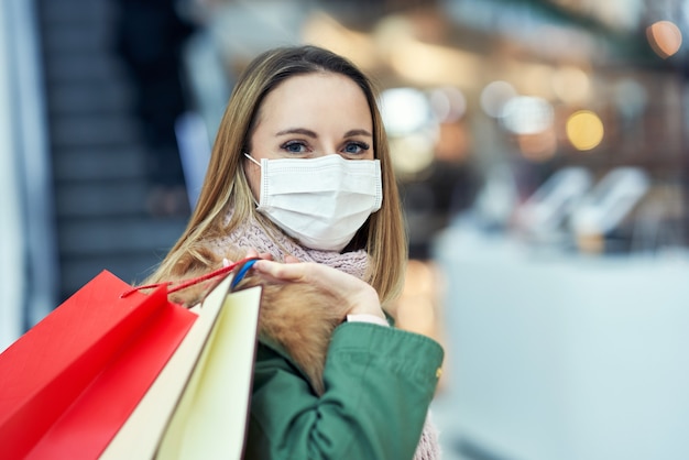 volwassen vrouw die in winkelcentrum winkelt met een masker, coronavirusconcept