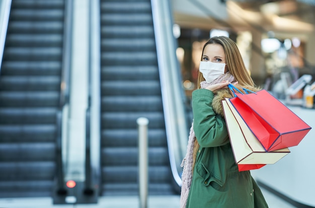 volwassen vrouw die in winkelcentrum winkelt met een masker, coronavirusconcept