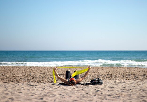 Volwassen vrouw die met elastiekjes op het strand traint die op het strand ligt