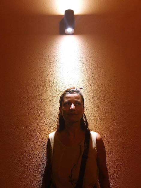 Foto volwassen vrouw die onder verlichte verlichtingstoestellen aan de muur staat