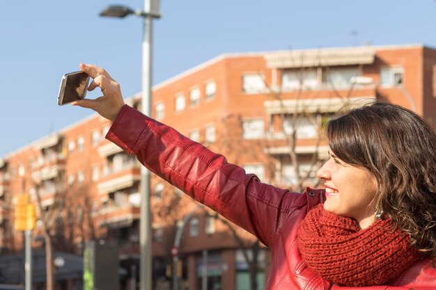Foto volwassen vrouw die selfie maakt met haar mobiele telefoon terwijl ze tegen een gebouw in de stad staat