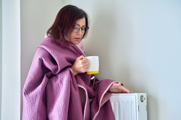 Volwassen vrouw die zichzelf opwarmt met deken verwarming radiator hete thee