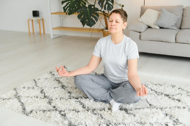 Volwassen vrouw doet fitnessoefeningen thuis senior vrouw doet rekoefeningen rijpe vrouw doet yogahoudingen