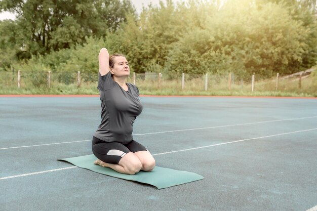 Volwassen vrouw doet yoga-asana's buiten in het stadion