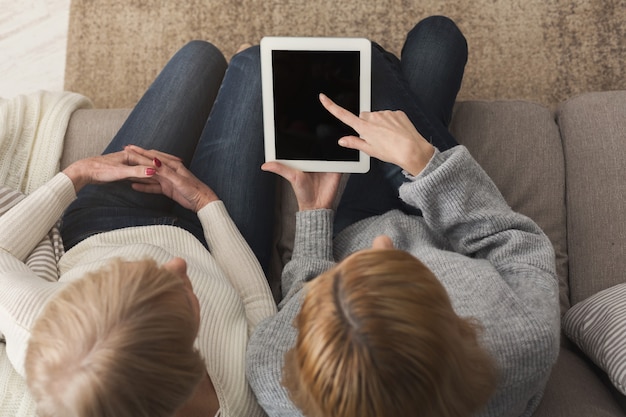 Volwassen vrouw en dochter met behulp van digitale tablet met leeg scherm voor reclame, kopieer ruimte. Vrouw die erop wijst. Generatie, relatie, modern technologieconcept, bovenaanzicht