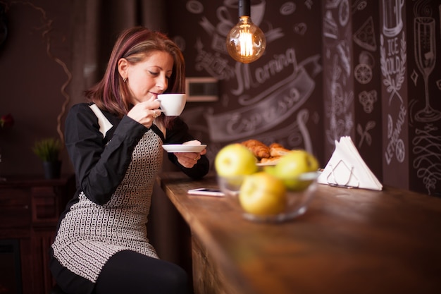 Volwassen vrouw geniet van haar kopje koffie aan de toog. Vrouw ontspannen in vintage coffeeshop