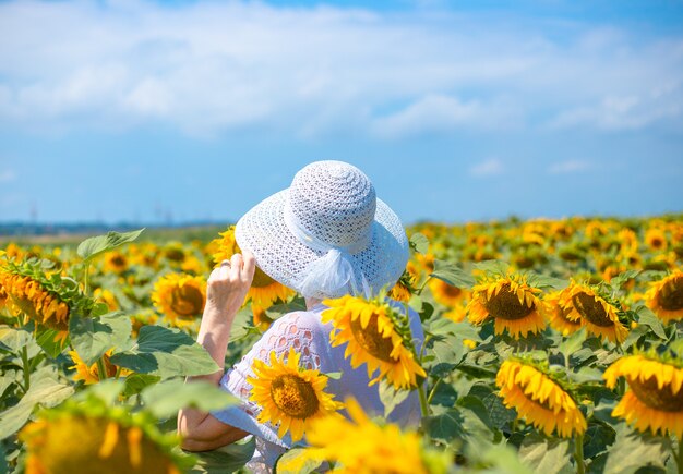 Volwassen vrouw in een hoed staat op een veld met bloeiende zonnebloemen en kijkt in de verte