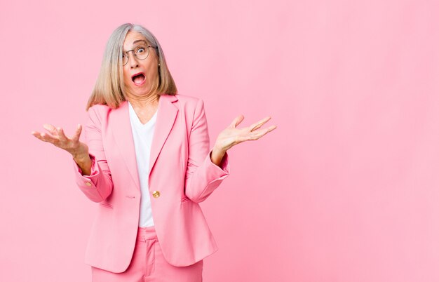 volwassen vrouw in roze pak met open mond en verbaasd